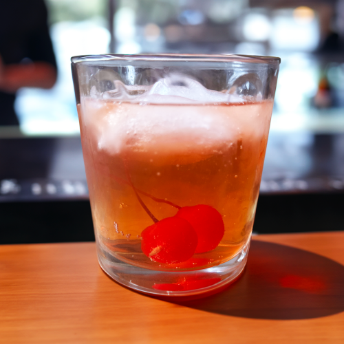 A Wisconsin old fashioned with two maraschino cherries sitting on a bar top.
