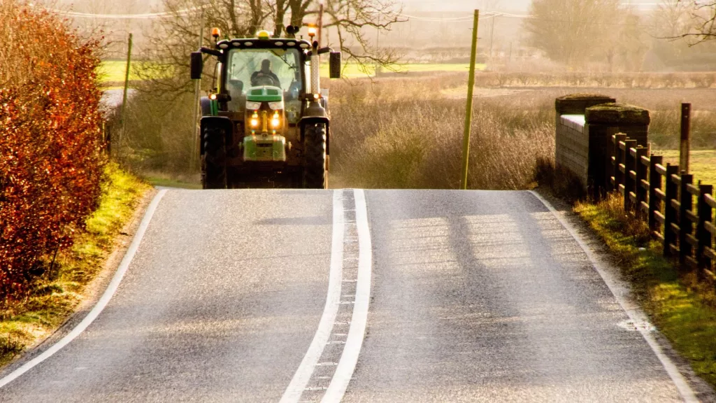 A tractor is driving toward the camera on a rural road in a no-passing zone.