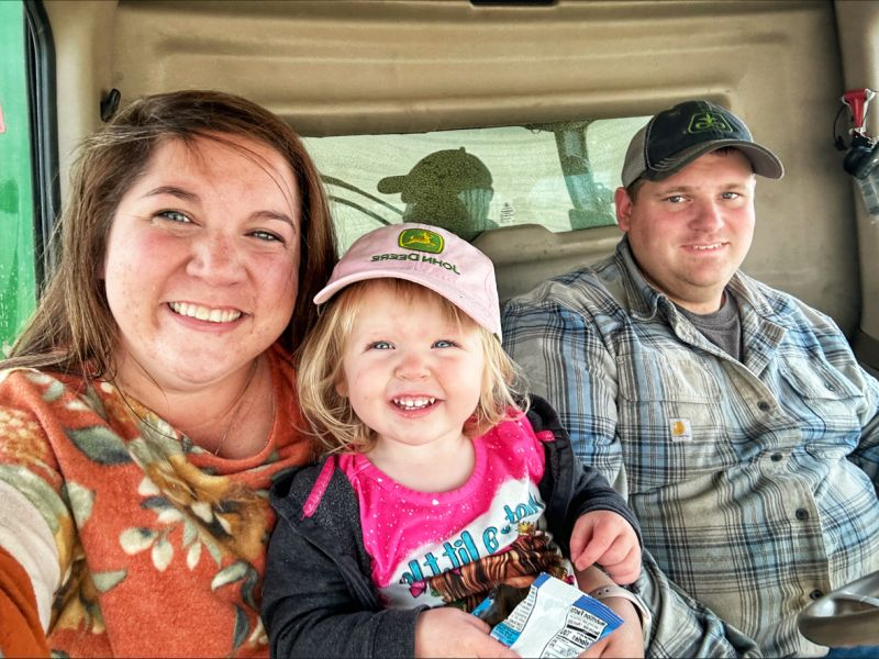 A farm mom, daughter and dad in the cab of a combine harvester.