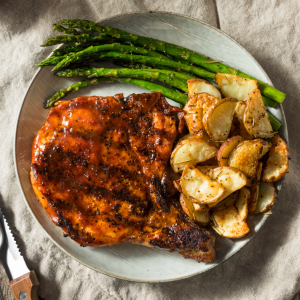 A dinner plate with grilled asparagus, potatoes and pork chops with a maple syrup glaze